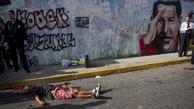 Un cadáver yace sobre el asfalto junto a un mural con la efigie de Hugo Chávez en una calle de Caracas, en una imagen de septiembre de 2010