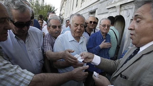 El empleado reparte turnos a un grupo de pensionistas frente a una sucursal del Banco Nacional de Grecia en el centro de Atenas