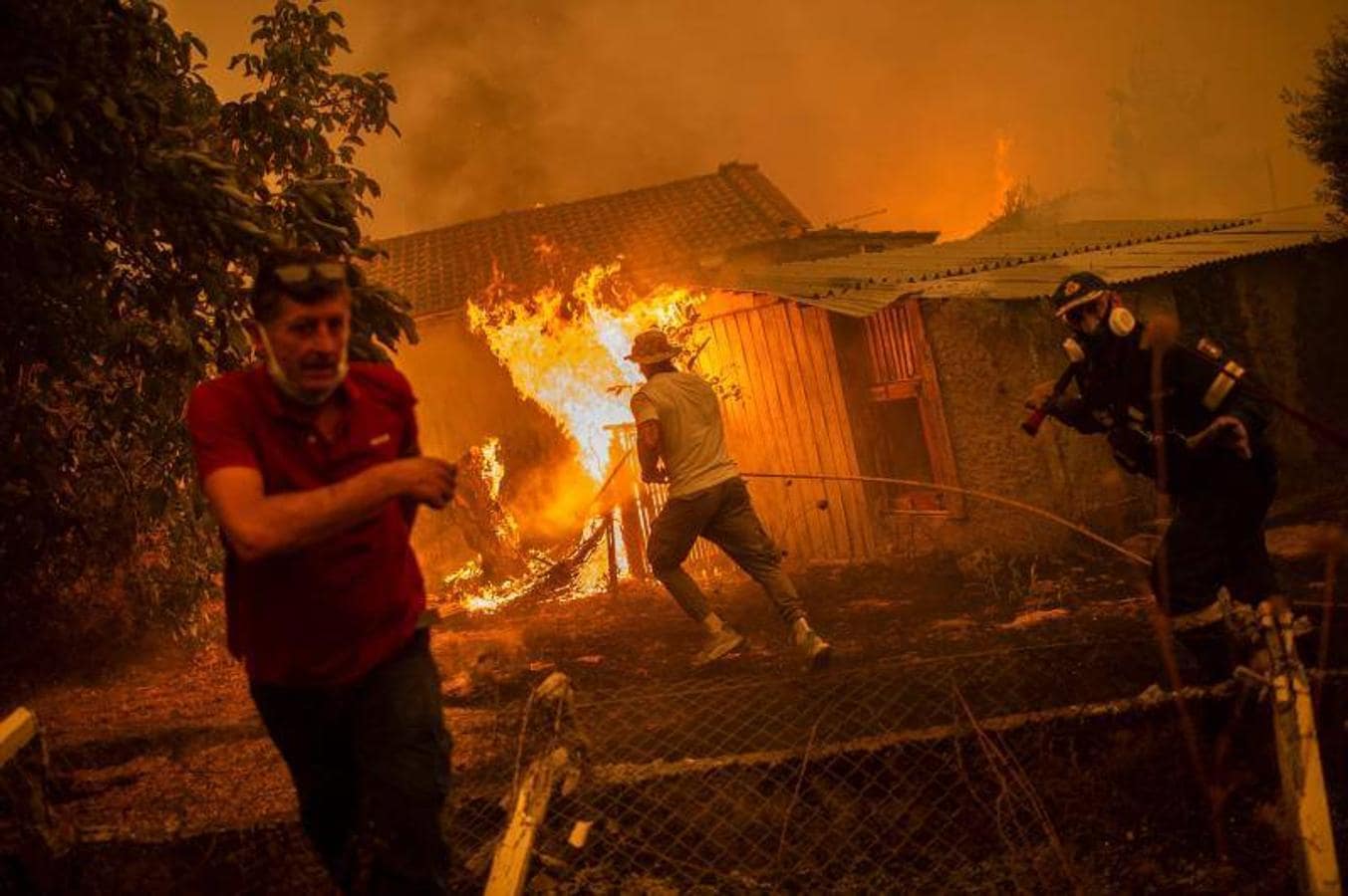 Un bombero y lugareños se apresuran a una casa en llamas en un intento de extinguir los incendios forestales que se acercan al pueblo de Pefki en la isla de Evia (Eubea)