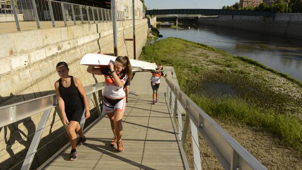 Varios alumnos de una escuela de remo sacan una barca del río, con el caudal a un nivel mínimo