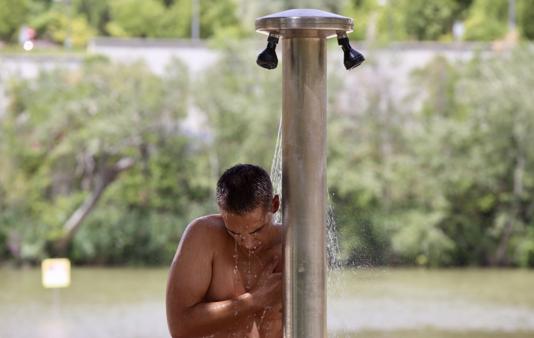 Un jóven refrescándose en la ducha de la playa de las Moreras en Valladolid