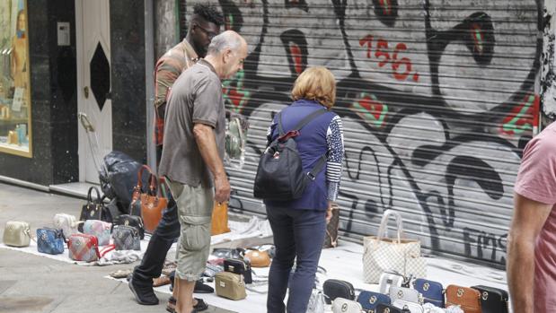 Uno de los manteros que frecuenta la calle Real de La Coruña, con una pareja que mira la mercancía