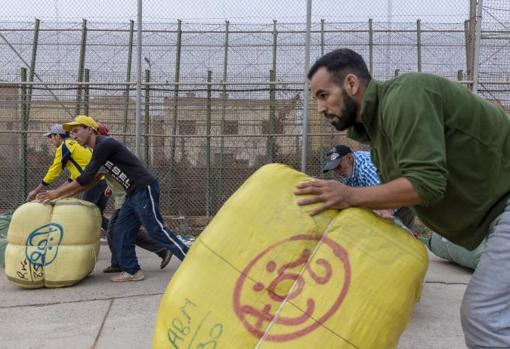 Varios porteadores arrastran los fardos junto a la valla de Melilla