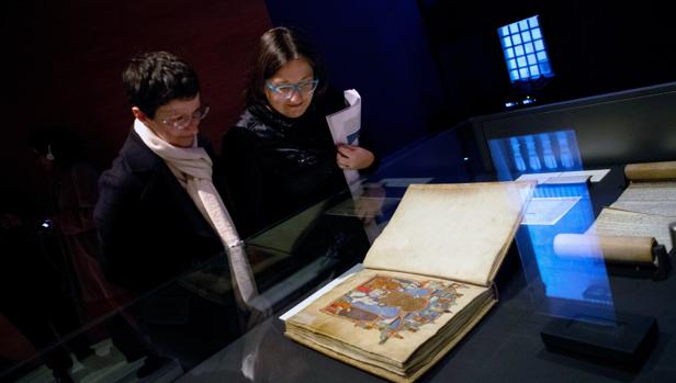 Dos visitantes observan el Gran Libro de los Feudos, un cartulario de documentos relativos a las relaciones feudales de los reyes de Aragón y condes de Barcelona