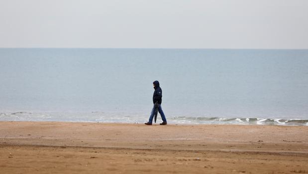 Un hombre se protege de la lluvia en una playa de Valencia