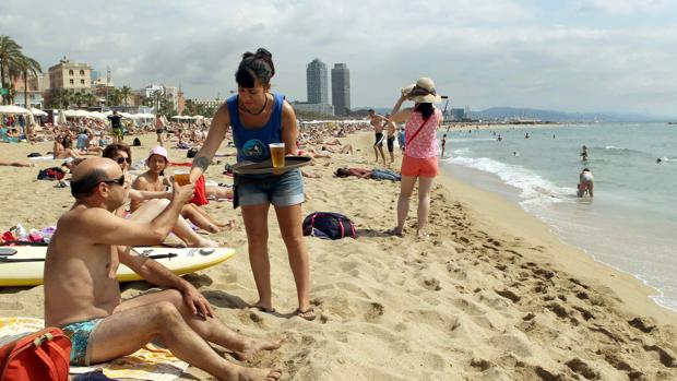 Una camarera de un chiringuito de la playa de la Barceloneta sirve una cerveza en la orilla