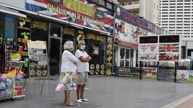 Una pareja de turistas junto a varios establecimientos de hostelería y comercio en Benidorm