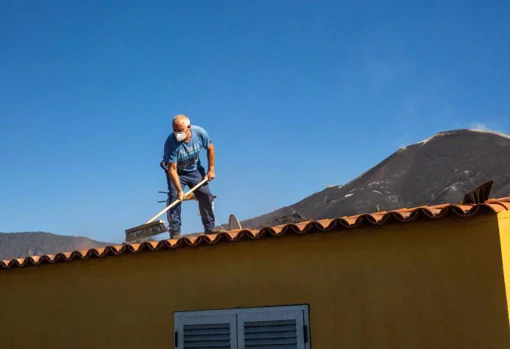 Neighbor cleans ash on the roof of his house in Las Manchas