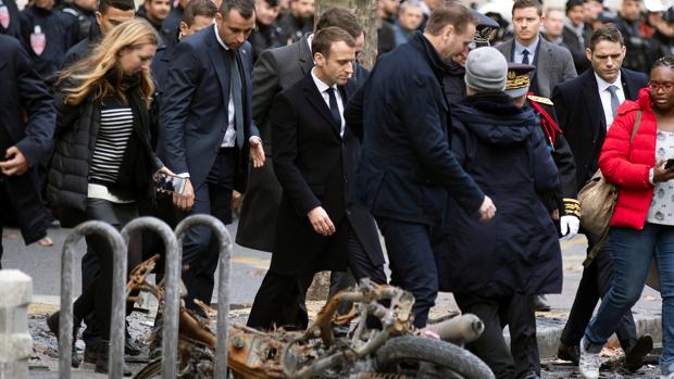 El presidente francés, Emmanuel macron (c), pasa junto a una motocicleta calcinada mientras comprueba personalmente los daños materiales ocasionados en las protestas de los llamados «chalecos amarillos»