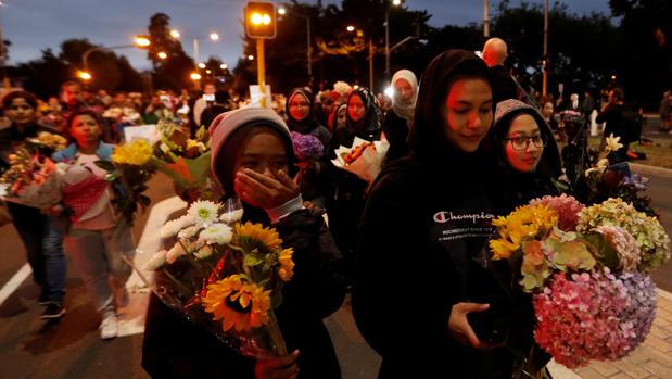 Un grupo de personas con flores avanza tras retirarse un cordón policial frente a la mezquita Al Noor