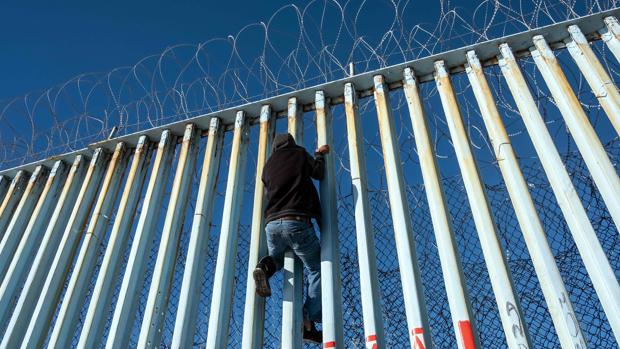 Un centroamericano escala por la valla que separa Estados Unidos y México en Tijuana