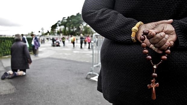 Una mujer sostiene un rosario mientras otra camina de rodillas durante la peregrinación anual al Santuario católico de Fátima en Portugal, este jueves 12 de mayo