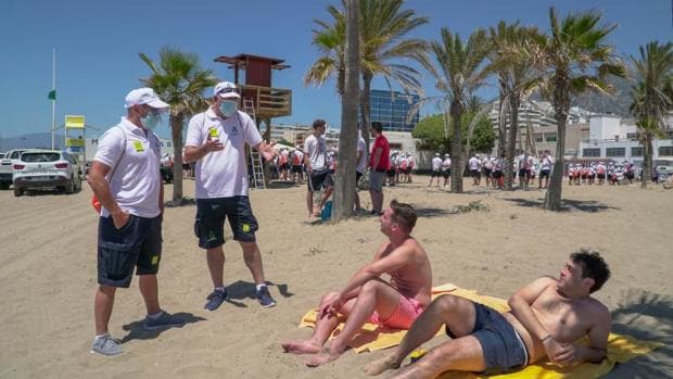 Dos auxiliares informan a unas personas sentadas en la arena de la playa de Marbella (Málaga) sobre las medidas de seguridad